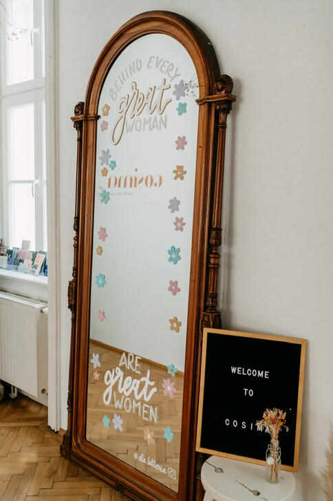 Das Bild zeigt einen Spiegel, der mit Blumen und einem Spruch bemalt ist.