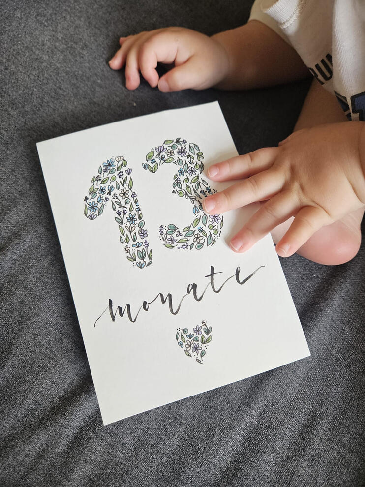 Das Bild zeigt eine Karte mit "13 Monate" und ein Baby.